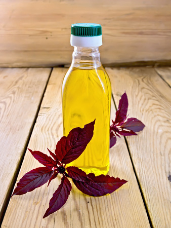 One plastic bottle of oil with a branch burgundy amaranth on background light wooden boardsの写真素材
