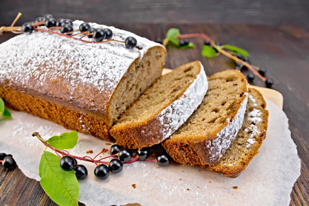 Fruitcake bird cherry cut with berries on a paper on the background of the dark wooden boardの写真素材
