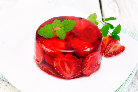 Strawberry jelly with mint and berries in a plate on a napkin on the background light wooden boardsの写真素材