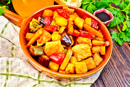 Roast of meat, zucchini, eggplant, carrot and sweet pepper with honey, soy sauce and red wine in a frying pan on a towel on the background of dark wood planksの写真素材