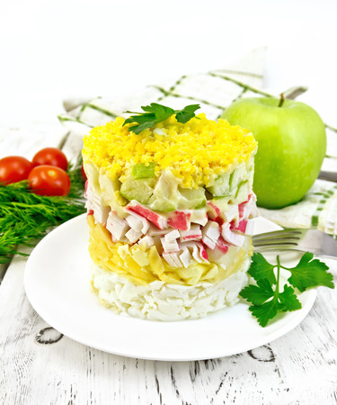 Salad of crab meat, cheese, eggs and green apple in the plate, napkin, dill on the background light wooden boardsの写真素材