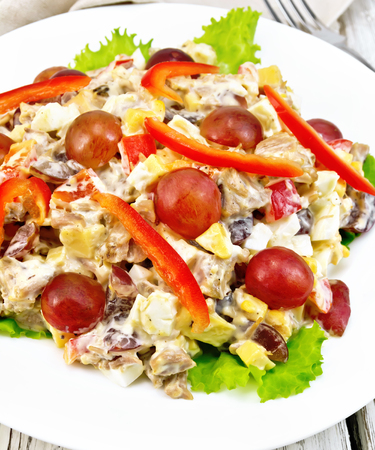 Salad of meat, salty soft feta cheese, sweet pepper, egg and grape with mayonnaise on lettuce in plate against the background of wooden boardsの写真素材