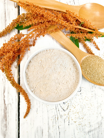 Flour amaranth in a bowl, a spoon with grain, brown flower with green leaves on the background of the wooden planks on topの写真素材