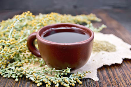 Herbal tea in a brown clay cup, twigs gray sagebrush, wormwood dried on a paper on the background of a wooden tabletopの写真素材
