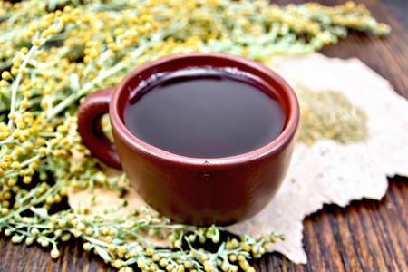 Herbal tea in a brown clay cup, twigs gray sagebrush, wormwood dried on a paper on the background of wooden boardsの写真素材