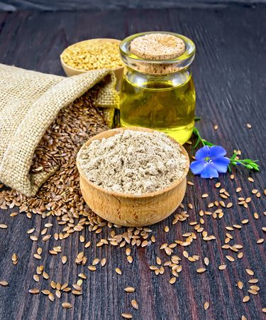 Flax flour in a bowl, seeds in a bag, blue linen flower and oil in a glass jar on a wooden board backgroundの写真素材