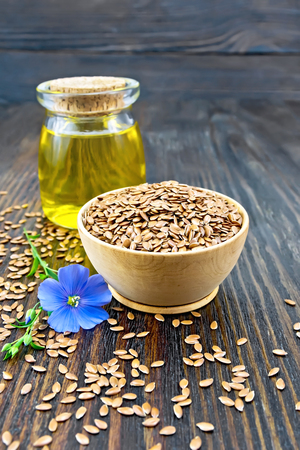 Seeds of linen brown in a bowl, linseed oil in a glass jar and flower on a background of a dark wooden boardの写真素材