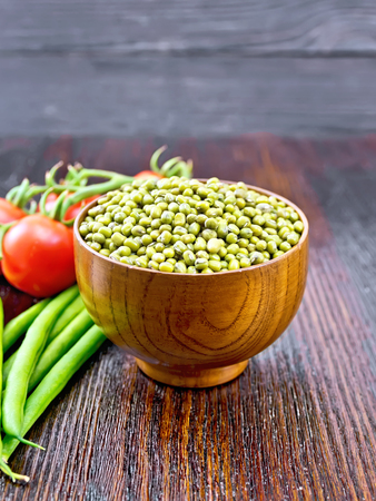 Green lentils mung in a bowl, pods of beans and red tomatoes on  a dark wooden boardの写真素材