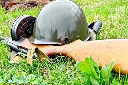 A helmet and a submachine gun of the times of the Great Patriotic War, a bag of protective color against green grassの写真素材