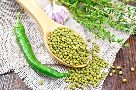 Green lentils mung in a spoon with hot peppers, garlic and thyme on sackcloth on a wooden board backgroundの写真素材