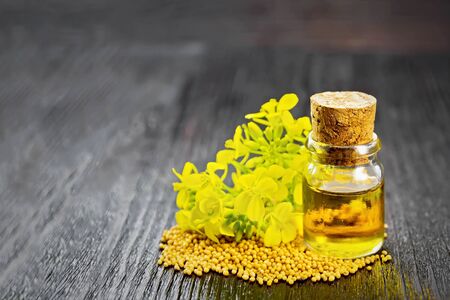 Mustard oil in a glass bottle, grains and yellow flowers on a wooden board backgroundの写真素材