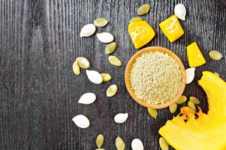 Pumpkin flour in a bowl, seeds on the table, slices of vegetable on dark wooden board background from aboveの写真素材