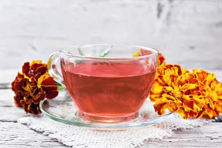 Marigold herbal tea in a glass cup and saucer on a napkin of sackcloth, fresh flowers on wooden board backgroundの写真素材