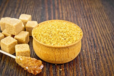 Granulated brown sugar in a bowl, crystalline on a stick and diced on wooden board backgroundの写真素材