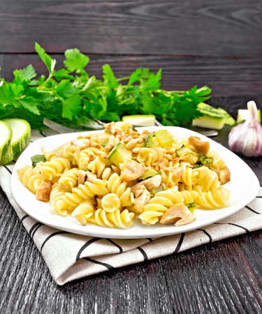 Fusilli pasta with chicken breast, zucchini, cream and pine nuts in a plate on napkin, garlic, fork and parsley on a wooden board backgroundの写真素材