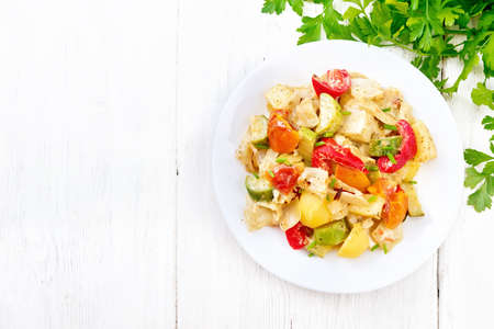 Vegetable ragout with zucchini, cabbage, potatoes, tomatoes and bell peppers in creamy sauce in plate, napkin, parsley and fork on wooden board background from aboveの写真素材
