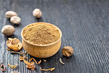 Ground nutmeg in a bowl, dried nutmeg arillus and whole nuts on a wooden board background