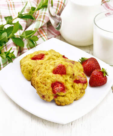 Strawberry scones in a plate with berries, a napkin, mint, milk in jug and glass on wooden board backgroundの写真素材