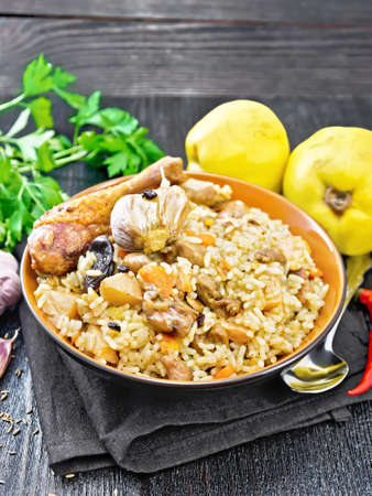 Pilaf from rice, duck, quince, carrots with garlic, onion, prunes and spices in a plate on a towel on wooden board backgroundの写真素材