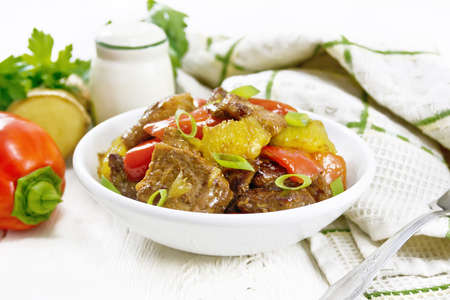 Beef with oranges, bell pepper and ginger root in a bowl, towel and a fork on wooden board backgroundの写真素材