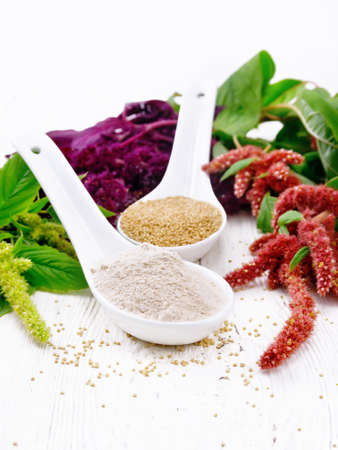 Flour and seeds amaranth in two spoons, brown, green and purple flowers and leaves of a plant on the background of light wooden boardの写真素材