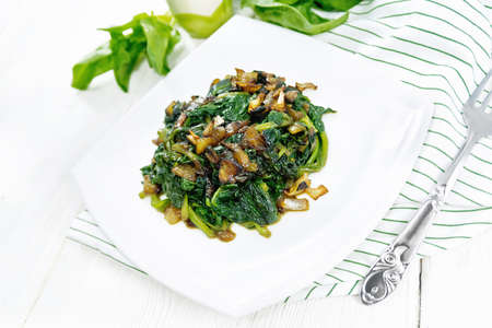 Spinach fried with onions in a plate on a towel against the background of wooden boardの写真素材