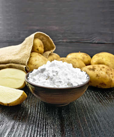 Potato starch in clay bowl, vegetable tubers in a bag and on the table against the background of black wooden boardの写真素材