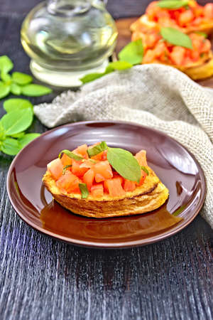 Bruschetta with tomatoes and basil in a plate, napkin and vegetable oil in a decanter on wooden board backgroundの写真素材