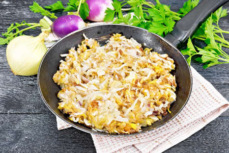 Fried turnips with onions in a frying pan on a towel on black wooden board backgroundの写真素材