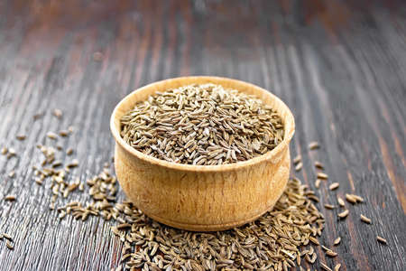 Cumin seeds in a bowl and on a table against dark wooden board backgroundの写真素材