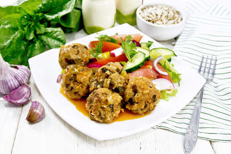 Minced meatballs with spinach, oatmeal and green onions in tomato sauce, vegetable salad in a plate, napkin on the background of a light wooden boardの写真素材