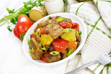 Beef with oranges, bell peppers and ginger root in bowl, a napkin and a fork on white wooden board backgroundの写真素材