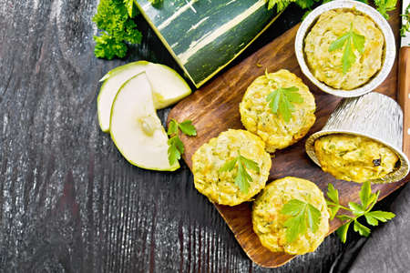 Small cheese and zucchini muffins with herbs, parsley, thyme, knife and towel on a dark wooden board background from aboveの写真素材