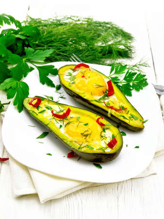 Scrambled eggs with hot peppers in two halves of avocado in a plate on a towel, fork, parsley on a wooden board backgroundの写真素材