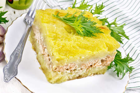 Mashed potato casserole with salmon fillet and lettuce in a plate, towel, garlic on the background of a light wooden boardの写真素材