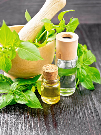 Oil with basil in two vials, mortar and basil leaves on a dark wooden board backgroundの写真素材