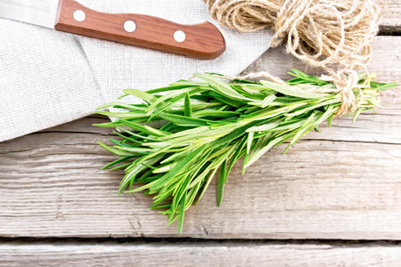 Bunch of fresh rosemary tied with twine, skein of rope, a napkin and a knife on wooden board background from aboveの写真素材