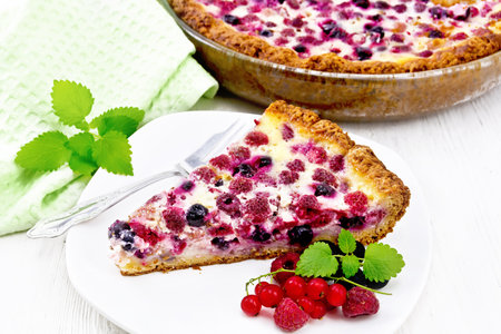 Pie with raspberries, currants and cream sauce in a plate, towel and mint on the background of light wooden boardの写真素材