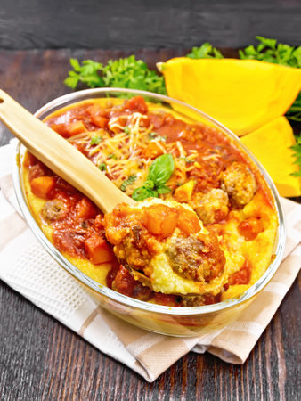 Corn porridge with meatballs, sauce of tomato, garlic and pumpkin, sprinkled with cheese, basil and spoon in a pan on towel on wooden board backgroundの写真素材