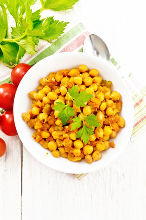 Chickpeas stewed with celery, tomatoes, onions, carrots and garlic in a plate on a napkin on the background of light wooden board from aboveの写真素材