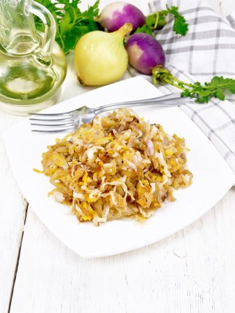 Fried turnips with onions in a plate, oil in decanter, napkin on wooden board backgroundの写真素材