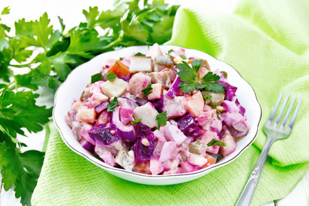 Finnish Rosoli salad of herring, beet, potatoes, pickled or pickled cucumbers, carrots, onions and eggs, dressed with mayonnaise in a bowl against light wooden boardの写真素材