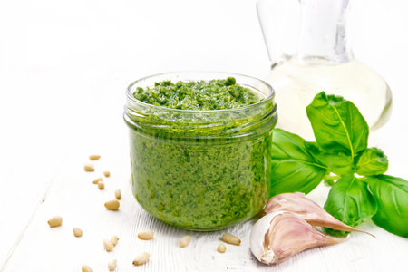 Pesto sauce in a glass jar, basil, pine nuts, garlic and olive oil on white wooden board backgroundの写真素材