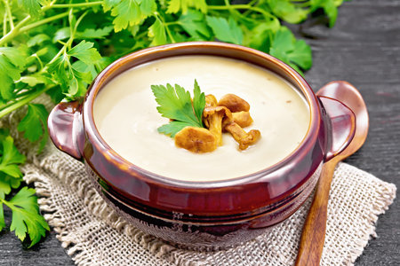 Soup puree from chanterelles, potatoes, onions and cream in a clay bowl on burlap, parsley and a spoon on wooden board backgroundの写真素材