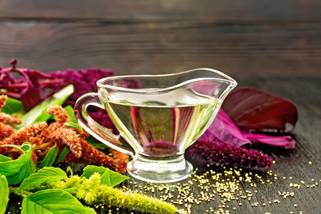 Amaranth oil in a glass gravy boat, brown, green and purple flowers and leaves of the plant on the background of a wooden boardの写真素材
