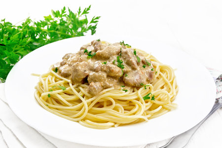 Pieces of meat in creamy sauce with spaghetti in a plate on a towel against the background of wooden boardの写真素材