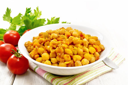 Chickpeas stewed with celery, tomatoes, onions, carrots and garlic in a plate on a kitchen towel on wooden board backgroundの写真素材