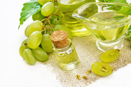 Grape oil in a bottle, gravy boat and a jar on sacking, berries and seeds of green grapes on wooden board backgroundの写真素材