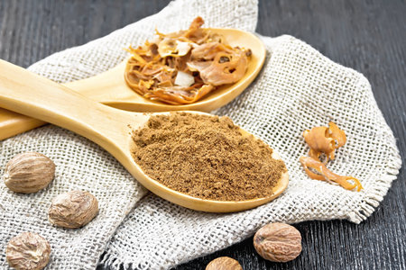 Ground nutmeg and dried nutmeg arillus in two spoons, whole nuts on burlap on a wooden board backgroundの写真素材
