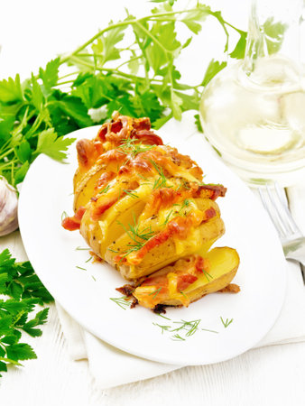 Baked potatoes layered with smoked bacon and cheese in a plate on a towel against white wooden board backgroundの写真素材